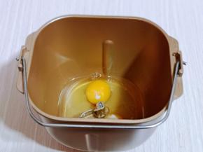 首先将玉米油与鸡蛋加入面包桶中。