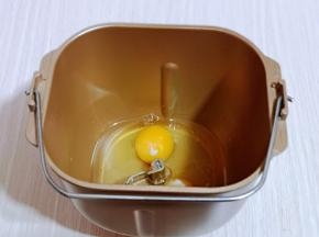 首先将玉米油与鸡蛋加入面包桶中。