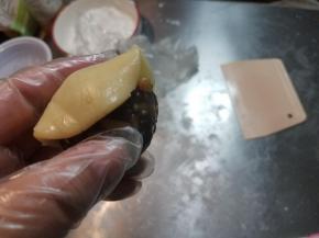 取出一块面团，搓成圆球状，用刮板压扁，拿起来放到一只手的虎口处，手上沾少许面粉，再把准备好揉成圆球的馅料放在面饼的中心处，用皮包住馅料，一点一点往上推，手一定要轻，不要露陷，尽量做到面皮均匀。