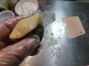 取出一块面团，搓成圆球状，用刮板压扁，拿起来放到一只手的虎口处，手上沾少许面粉，再把准备好揉成圆球的馅料放在面饼的中心处，用皮包住馅料，一点一点往上推，手一定要轻，不要露陷，尽量做到面皮均匀。