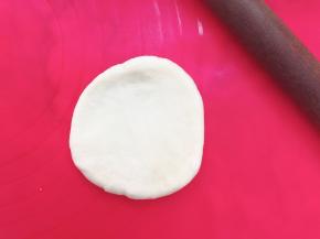 取一个面团，用擀面杖擀成中间厚边上薄的圆形，借助刮板把面团翻面