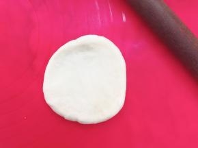 取一个面团，用擀面杖擀成中间厚边上薄的圆形，借助刮板把面团翻面