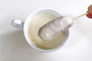 把面糊倒入一个小杯子中，把穿有牙签的香肠放入杯子蘸一下挂上面糊。