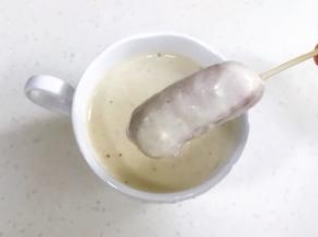 把面糊倒入一个小杯子中，把穿有牙签的香肠放入杯子蘸一下挂上面糊。