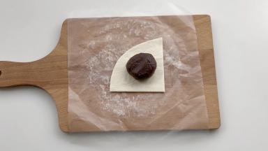 把25克左右的红豆沙馅放在1/4的飞饼皮上，注意留出边缘。