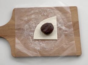 把25克左右的红豆沙馅放在1/4的飞饼皮上，注意留出边缘。