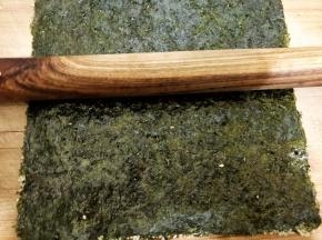 再取一张海苔在粗糙面刷上酱汁后，跟有芝麻的海苔重合在一起，用擀面杖擀压让两片海苔贴合更紧