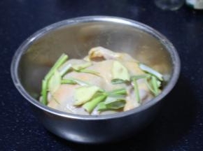 将姜片和葱段放入腌制童子鸡的盆里。