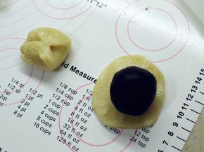 取一份松弛好的面团，从中间按压下去，将两头按到中间，用擀面杖擀成中间厚四周薄的圆形。放上包好的豆沙蛋黄馅。