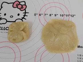 取一份松弛好的面团，从中间按压下去，将两头按到中间，用擀面杖擀成中间厚四周薄的圆形。
