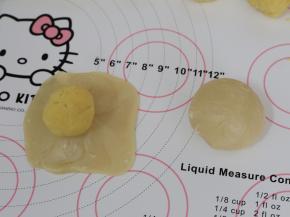 放上绿豆馅。翻过来，将皮收一下，让它紧贴着馅料。一手大拇指按住馅料，另一手虎口往上推饼皮，使它紧贴着馅料并慢慢地往上爬，最后收口。