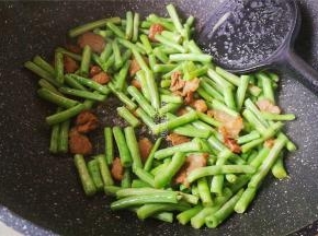 炒制片刻后，倒入料酒，生抽继续翻炒下，豇豆洗净切小段倒入锅中跟肉一起翻炒。