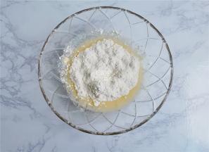 把低筋面粉筛入混合好的液体中，把泡打粉和苏打粉也放入，用刮刀混合均匀。