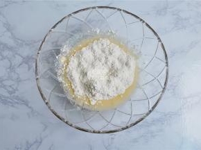 把低筋面粉筛入混合好的液体中，把泡打粉和苏打粉也放入，用刮刀混合均匀。