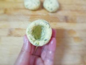 将圆锥形的面团放在左手手心里，用右手的大拇指放在圆锥形底部的中间位置，转圈旋出窝窝。