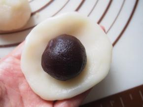 将冰皮放在手心压扁，放入豆沙藜麦馅包起来。