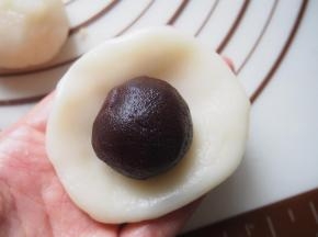将冰皮放在手心压扁，放入豆沙藜麦馅包起来。