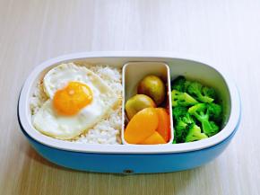 米饭装入便当盒中，放上爱心煎蛋，水果，西蓝花。