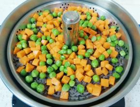 升降电火锅里面重新加入水，放上提篮，将准备好的胡萝卜和豌豆铺在糙米饭上面。