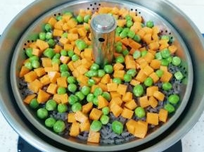 升降电火锅里面重新加入水，放上提篮，将准备好的胡萝卜和豌豆铺在糙米饭上面。