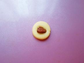 取一个搓好的小圆球压扁，再取一块碧根果仁蘸上蛋液，放在压扁的饼干面团中间，轻轻按压一下，一个碧根果曲奇饼干就做好了。