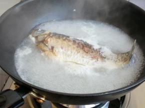 把一面煎黄后，再翻面煎另一面，煎鱼的时候少翻动，不要把鱼身煎碎。煎好后倒入没过鱼身的热水，倒入料酒，盖上锅盖