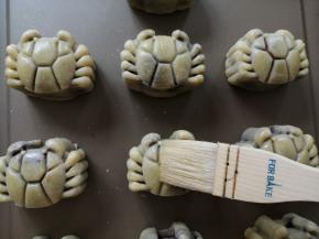 把月饼取出，用毛刷沾点蛋黄水（一个蛋黄+适量水，再过滤使用），在碗边轻扫一下，把多余的蛋黄水扫去，再刷月饼表面，侧面不用刷