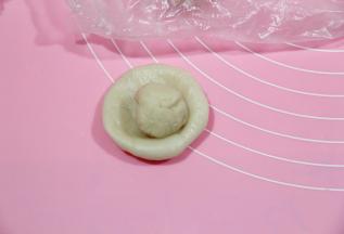 冷藏醒好的油皮，取出略回温一会，称一下油皮和油酥的重量，将油皮、油酥，每种分成12份。盖保鲜膜。防止油皮干掉。然后取一油皮，搓圆，然后放在左手掌心（我都是带PVC手套操作的），用右手掌心按扁，放上油酥。