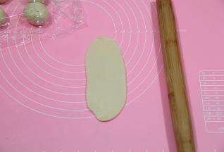 取一个包好的面团，收口朝上，按扁，用擀面杖从中间，往上或者往下擀开，不需要擀开太长，千万不要来回擀，动作轻柔一点。