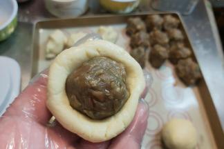 把面皮搓圆、压扁，包住馅料收拢滚圆。