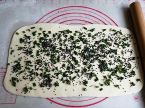 发酵好的面团揉搓排气，擀成长方形，在上面撒上葱花和芝麻