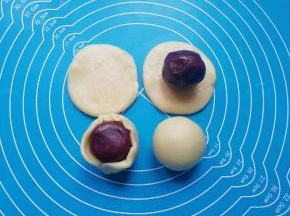 取一个擀好的饼皮，包入蛋黄豆沙馅，用虎口慢慢向上推挤收口，最后将收口朝下摆放，蛋黄酥就包好了。
