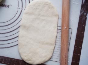 将面团擀成牛舌状，从一侧卷起来