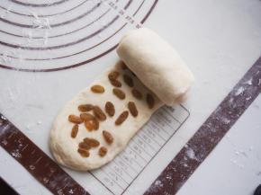 将面团再次擀开，放入提前浸泡清洗并沥干水分的葡萄干，从一侧卷起