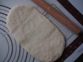 将面团擀成牛舌状，从一侧卷起来