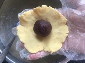 用手指将面饼边缘稍微捏薄，中间厚边缘薄，取一颗豆沙放至饼皮中心处；