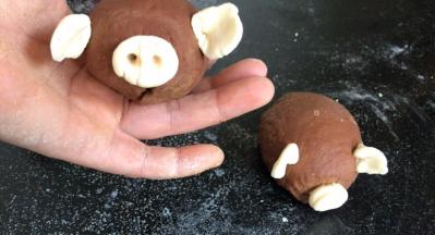 用白面团做成猪耳朵、嘴巴装在椭圆面团上，用筷子在猪嘴上插出鼻孔