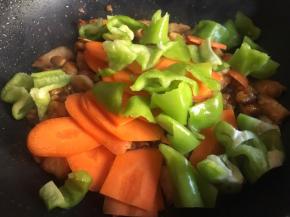 继续倒入胡萝卜片、青椒块，不停翻炒，翻炒至变色变软，大概8分熟；