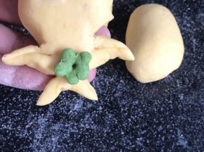 用绿色面团做一朵小花，贴在肚子中间