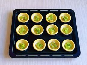 把蛋挞皮摆放在烤盘中，并间隔距离，再把切好的猕猴桃放入每个蛋挞皮里。