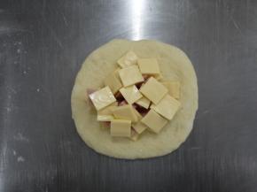面团松弛好后排气，用擀面棍擀平，放上芝士和火腿丁。