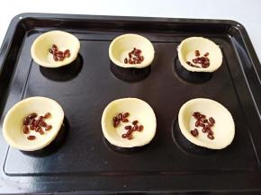 将蛋挞皮放在烤盘上摆放好，每个挞皮中放入几粒蜜豆。