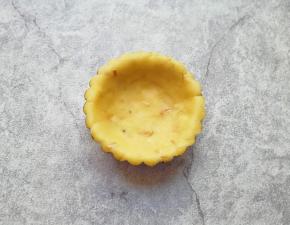 取一个小面团用手掌压扁，放入蛋挞模具里面，压成小碗状。
