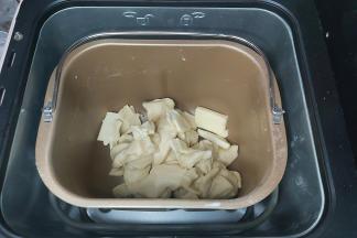 取出面团切成小块或者用剪刀剪成小块，同时把软化好的黄油也一并放入面包桶内，然后再放回面包机，再次设置一个MIX程序。