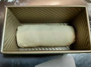 从上往下卷起面团，尽量卷紧，收口处轻轻捏紧一下，摆入吐司模具。
