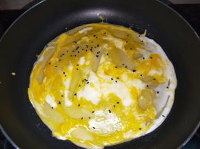 倒入一半面糊，摊平，面糊变色起泡的时候，磕入一个鸡蛋打散，撒上芝麻。