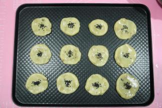 按扁，不需要按太扁，中间要留空，烘烤会膨胀，正好一盘12个。然后在面团中间位置刷一层全蛋液，撒上芝麻。