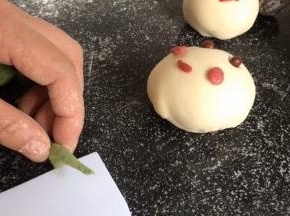 取少许绿面团搓成细长条，在中间切开，再在里侧压成饼皮，在里面压出叶子的纹路