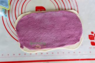 把紫薯面团叠加在白面团上面，并用擀面杖一起轻轻擀一下，让二种面团贴紧，从一头往上卷到另外一头。