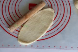 取一个中间发酵好的面团，用擀面杖擀成长椭圆形；